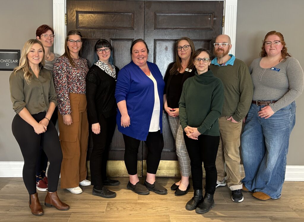 The Board of Directors stands in front of a wooden door outside a conference room. From left to right: Becky Bartley, RVT; Elise Ritter, RVT; Kelsey Streef, RVT; Amanda Borton, RVT; Jen Cote, RVT; Hailey Farkas, RVT; Ann McCallum, RVT; Wes Harris, RVT; Leslie Reid, RVT.