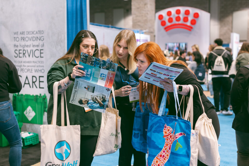 Three RVTs look at a map in the 2025 OAVT Conference Trade Show Hall, arms laden with bags and other swag.