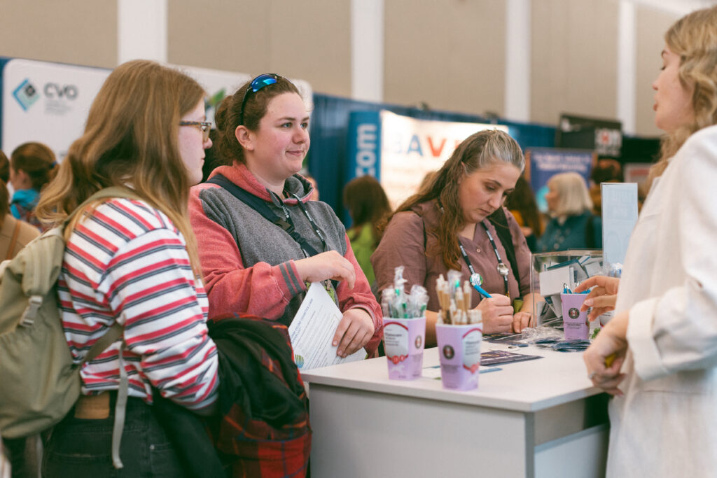 Two women speak with an exhibitor in the trade show at the 2026 OAVT Conference.